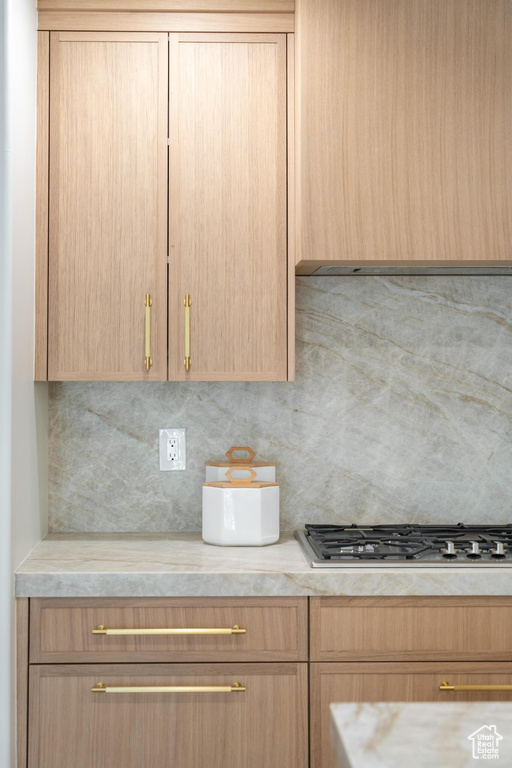 Kitchen with light countertops, backsplash, light brown cabinets, and stainless steel gas stovetop