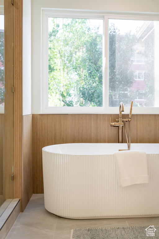 Bathroom with a freestanding tub, healthy amount of natural light, wood walls, a sink, and a wainscoted wall