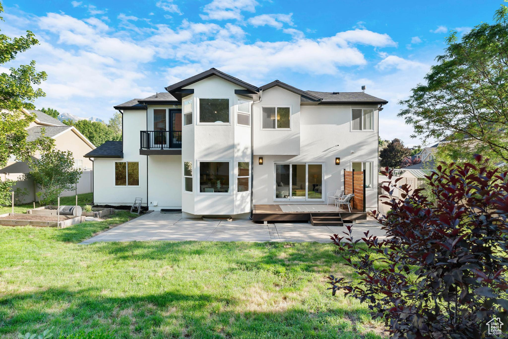 Rear view of property with a balcony, a patio, stucco siding, and a garden