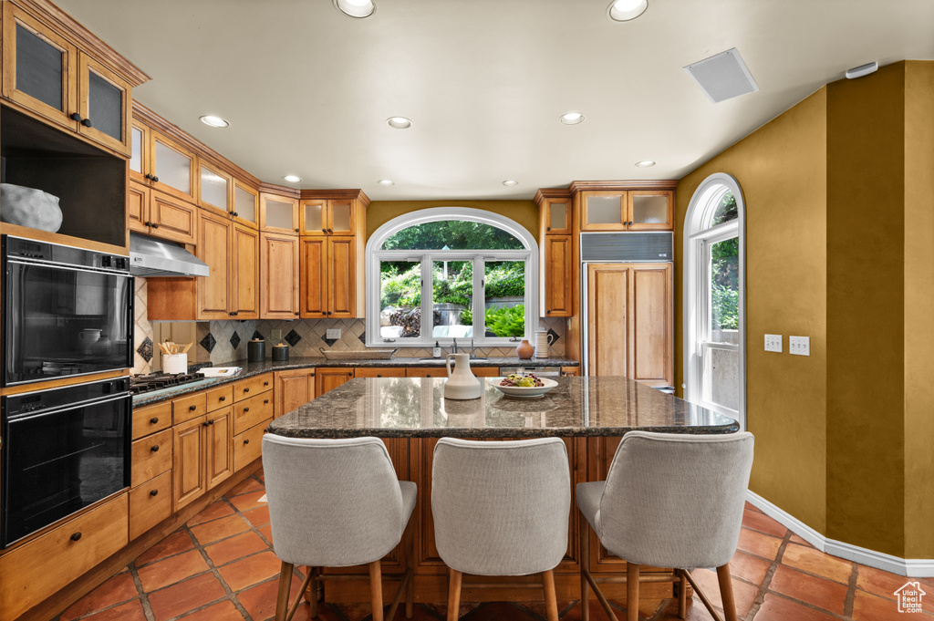 Kitchen featuring paneled built in fridge, decorative backsplash, a center island, under cabinet range hood, and a breakfast bar area