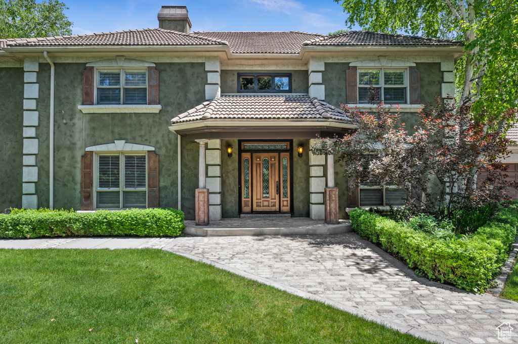View of front of house featuring a chimney, a tiled roof, stucco siding, and a front lawn