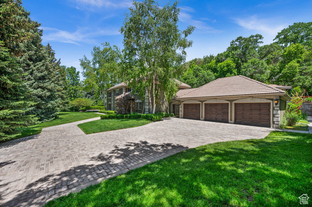 View of front facade featuring an attached garage, a front lawn, decorative driveway, a tile roof, and stone siding