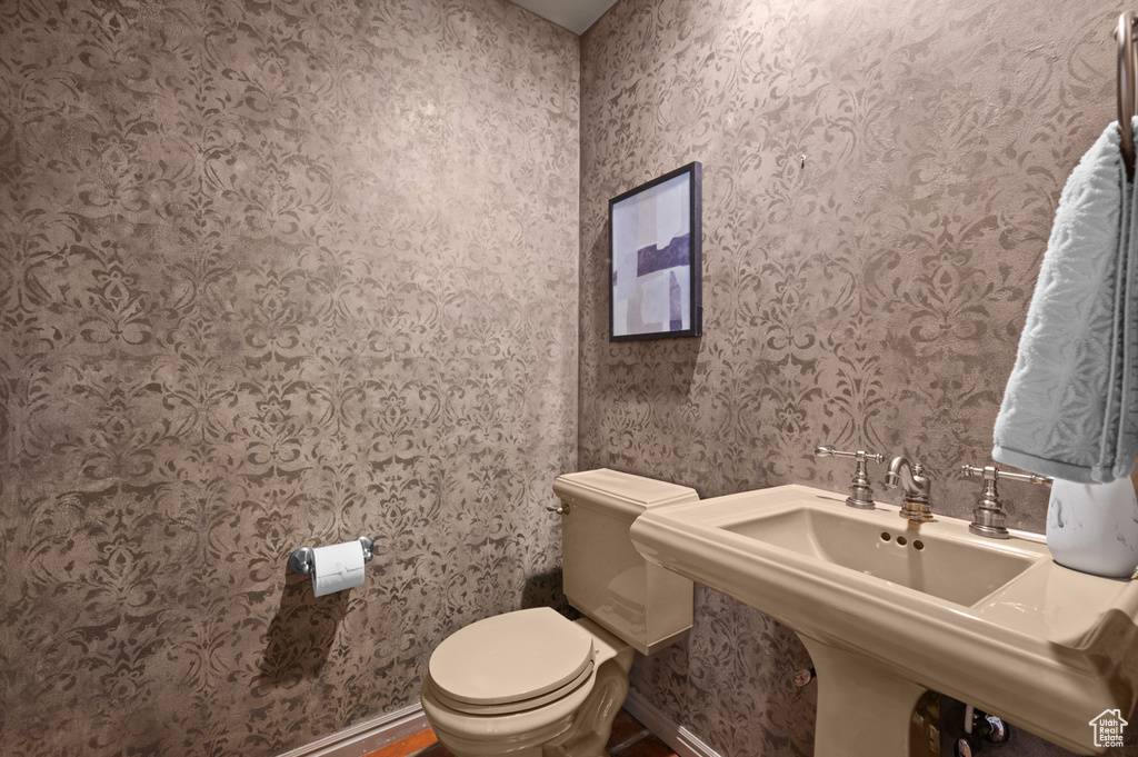 Half bathroom with toilet, baseboards, wallpapered walls, and a sink