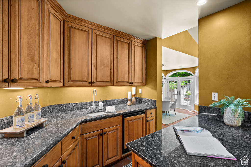 Kitchen with a sink, brown cabinets, dark stone counters, and french doors