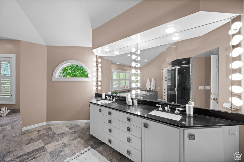 Bathroom featuring vaulted ceiling, double vanity, a shower stall, baseboards, and stone finish flooring