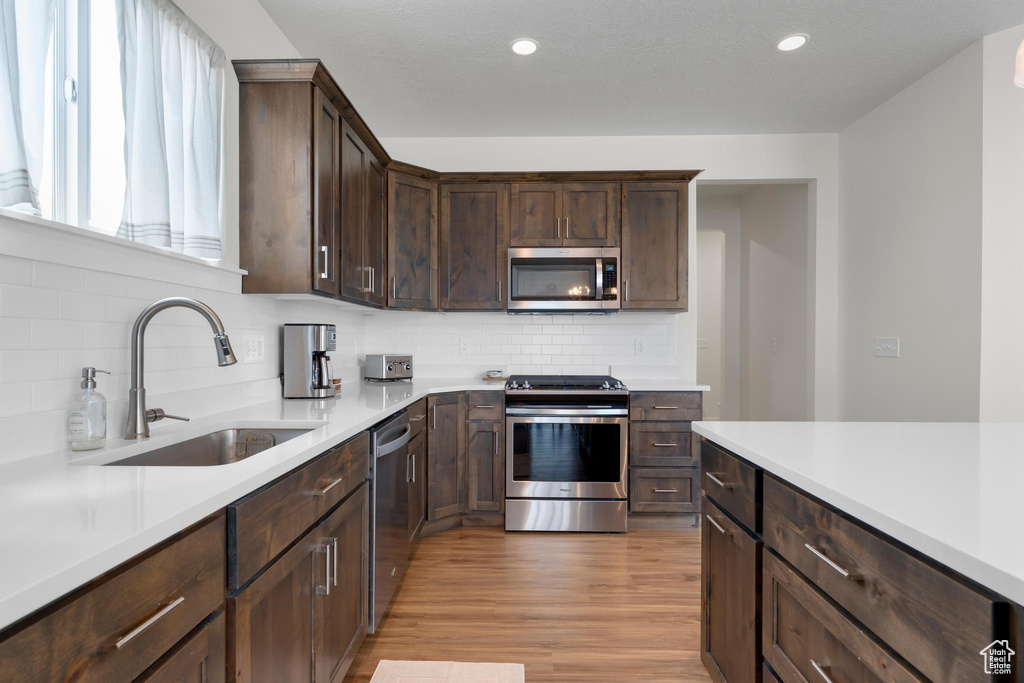 Kitchen featuring appliances with stainless steel finishes, a sink, light countertops, dark brown cabinets, and recessed lighting