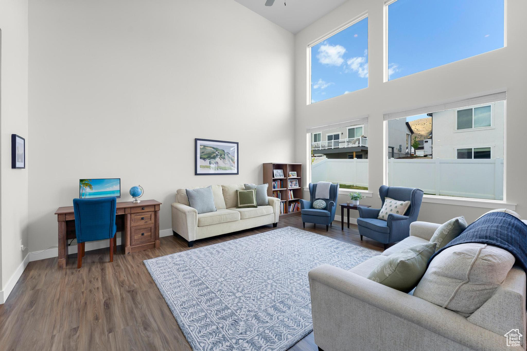 Living room featuring wood finished floors, a towering ceiling, baseboards, and a ceiling fan