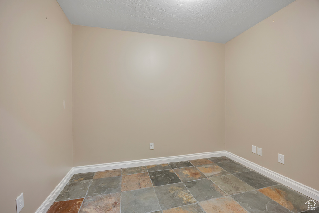 Empty room featuring stone tile floors, baseboards, and a textured ceiling