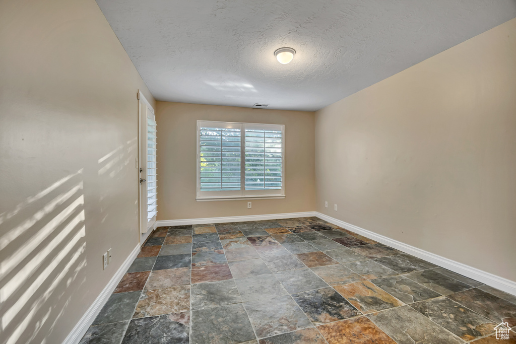 Spare room featuring stone tile floors, baseboards, and a textured ceiling
