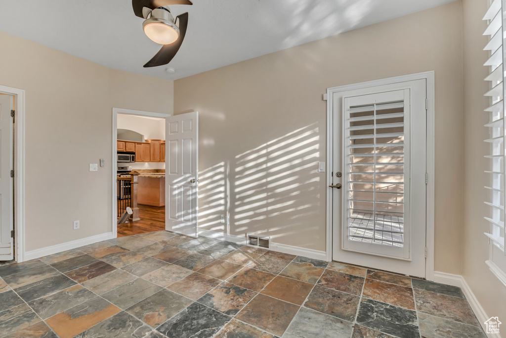 Empty room with ceiling fan, stone tile flooring, and baseboards