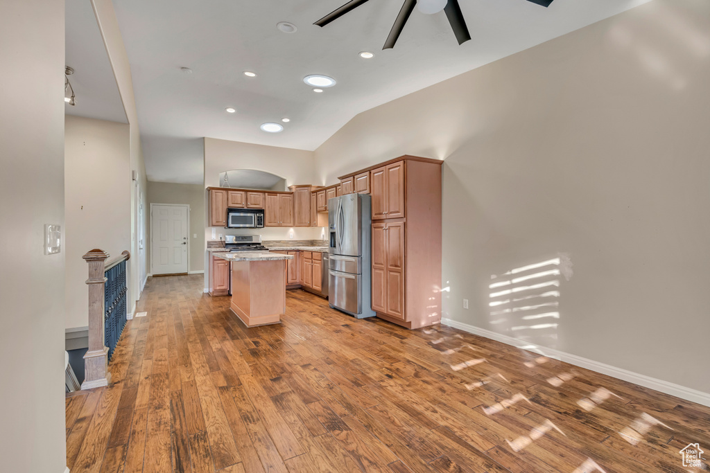 Kitchen with stainless steel appliances, ceiling fan, a center island, hardwood / wood-style floors, and baseboards