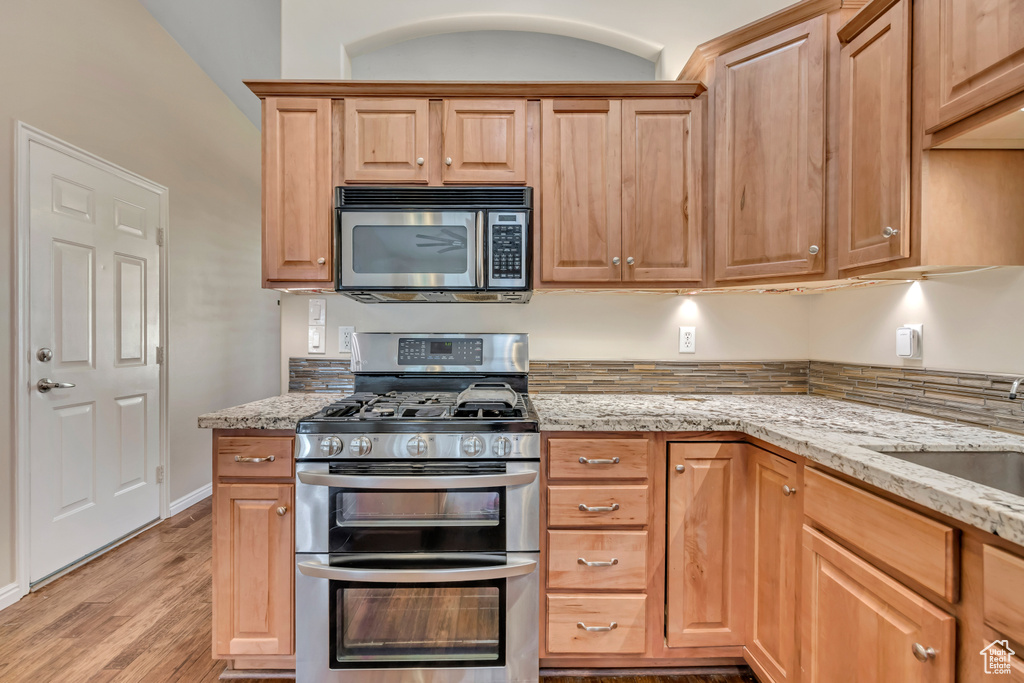 Kitchen with stainless steel appliances, light wood-type flooring, light stone countertops, and a sink