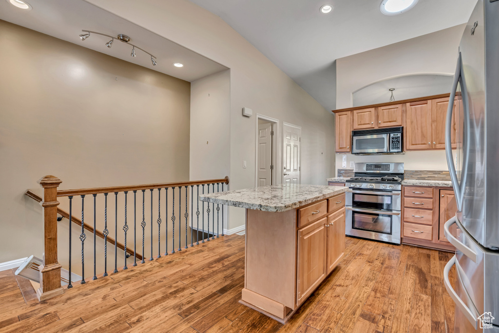 Kitchen with stainless steel appliances, light wood-type flooring, a center island, light stone counters, and recessed lighting