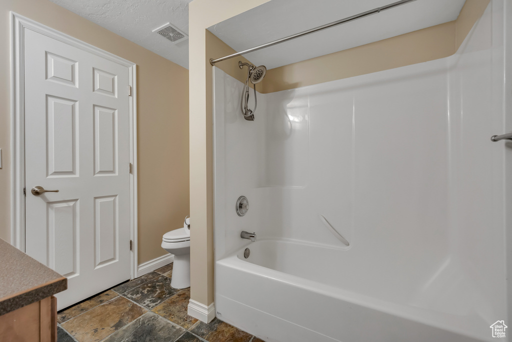 Bathroom with toilet, baseboards, shower / bath combination, vanity, and stone tile flooring