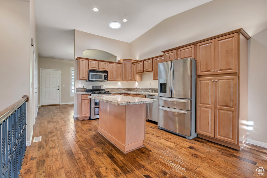 Kitchen featuring stainless steel appliances, a kitchen island, hardwood / wood-style floors, baseboards, and high vaulted ceiling