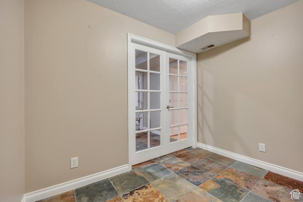 Spare room featuring stone tile floors, baseboards, french doors, and a textured ceiling