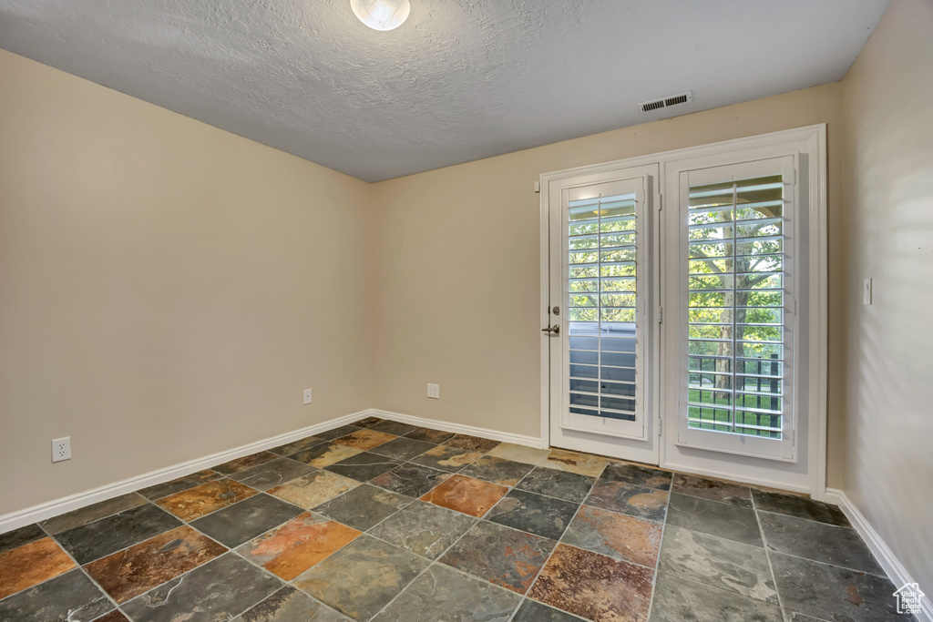 Empty room featuring stone tile flooring, baseboards, and a textured ceiling