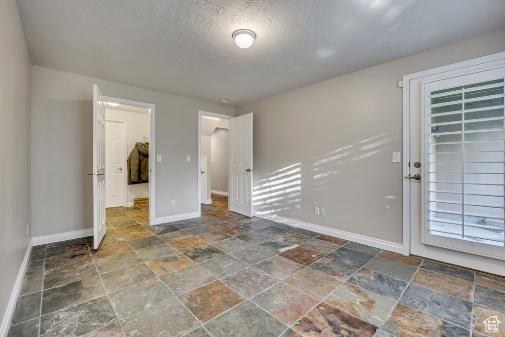 Unfurnished room with stone tile flooring, baseboards, and a textured ceiling