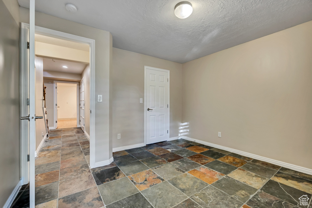 Unfurnished bedroom with stone tile flooring, baseboards, and a textured ceiling