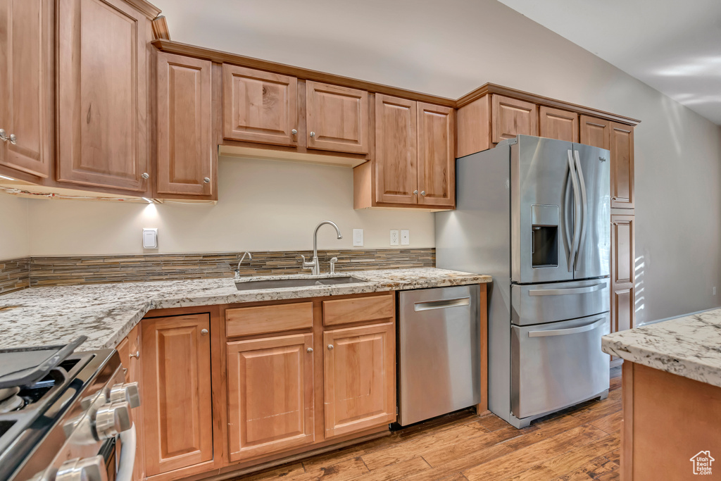 Kitchen featuring stainless steel appliances, a sink, light wood-style floors, and light stone countertops