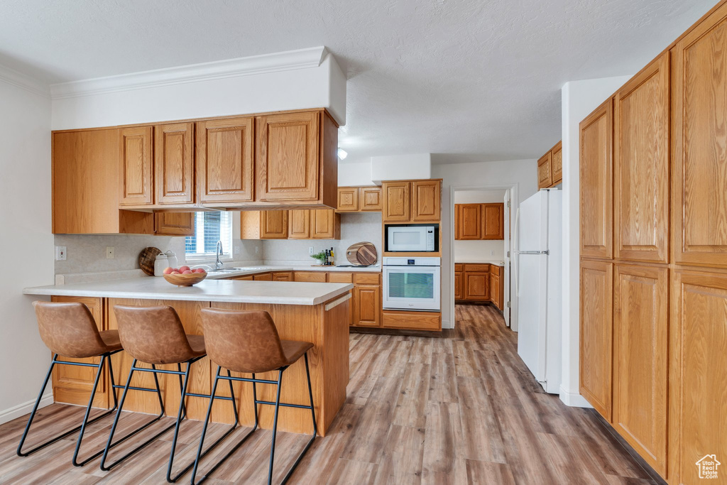 Kitchen with white appliances, a peninsula, light wood-style floors, a kitchen bar, and light countertops