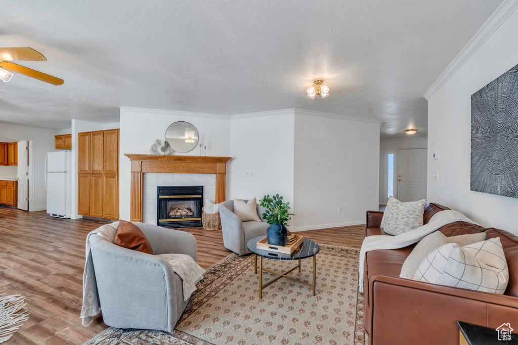 Living room with wood finished floors, ceiling fan, a tile fireplace, and ornamental molding