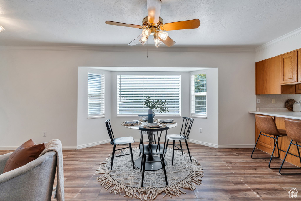 Dining area featuring ceiling fan, crown molding, light wood-style flooring, and a textured ceiling