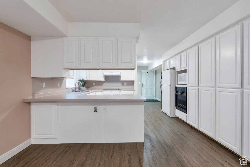 Kitchen featuring white appliances, light countertops, a peninsula, and dark wood-type flooring