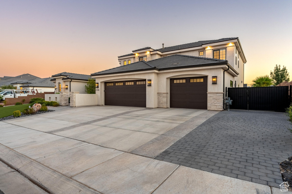 Prairie-style house with driveway, an attached garage, a gate, and stucco siding