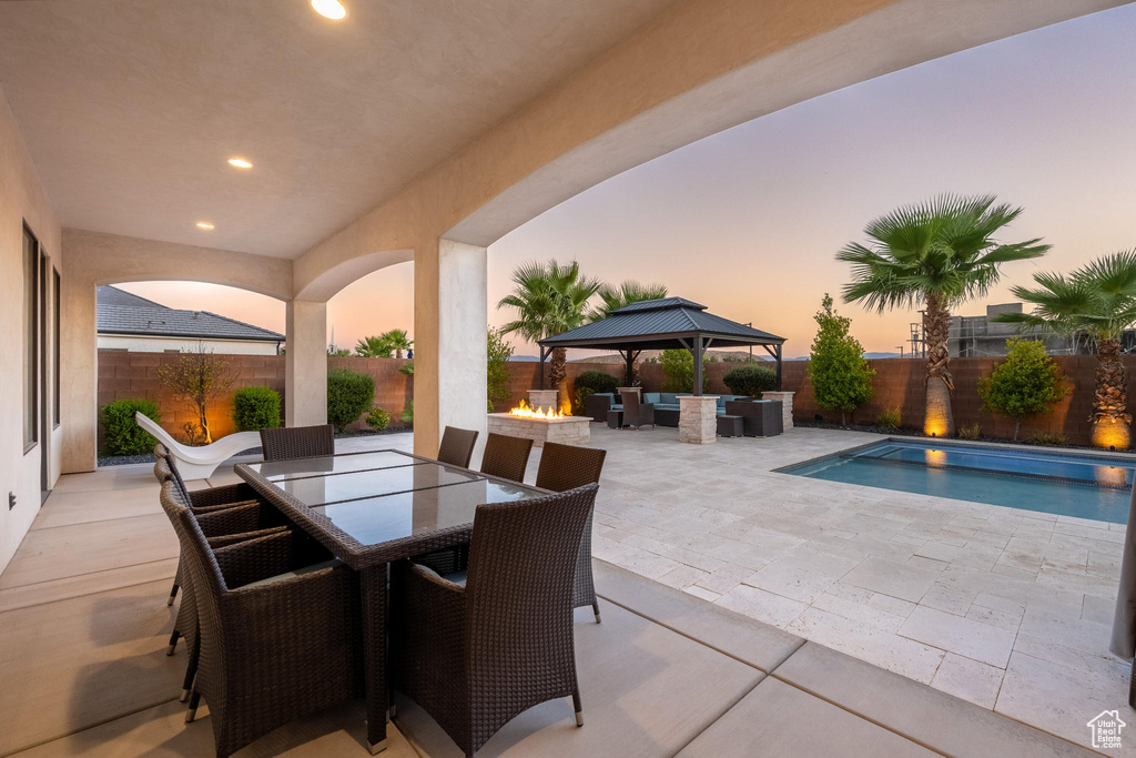 Patio terrace at dusk featuring a patio, outdoor dining area, a gazebo, a fenced backyard, and an outdoor living space with a fire pit