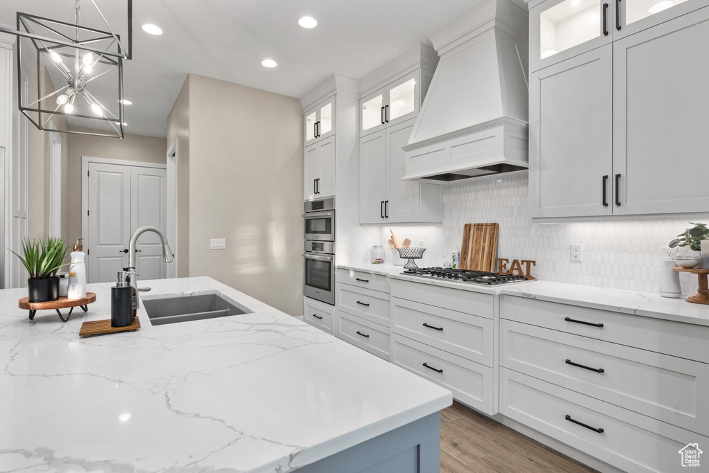 Kitchen featuring premium range hood, a chandelier, recessed lighting, decorative backsplash, and white cabinets