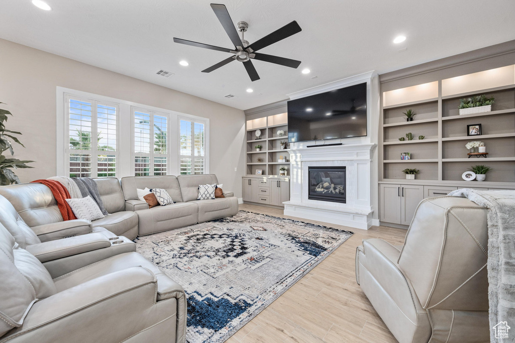 Living room with ceiling fan, light wood-style flooring, a glass covered fireplace, recessed lighting, and built in shelves
