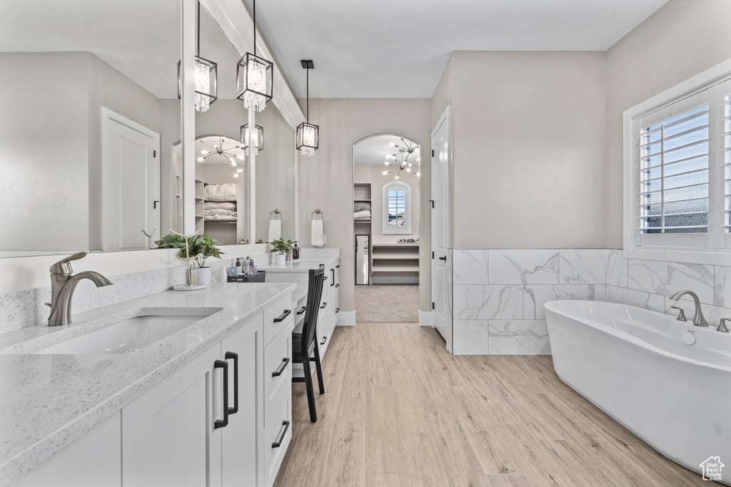 Ensuite bathroom featuring plenty of natural light, vanity, a soaking tub, and wood finished floors