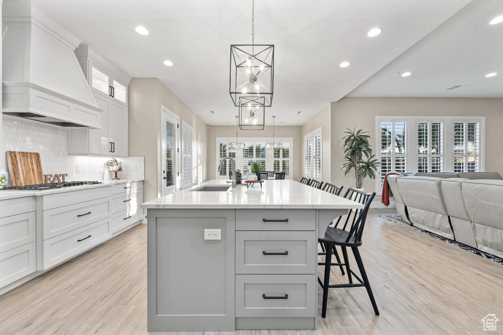 Kitchen with custom range hood, a chandelier, light wood finished floors, white gas stovetop, and recessed lighting