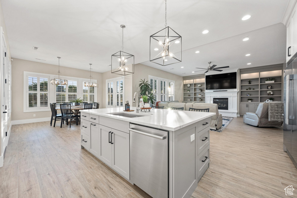 Kitchen featuring stainless steel dishwasher, a chandelier, ceiling fan, a kitchen island with sink, and a glass covered fireplace