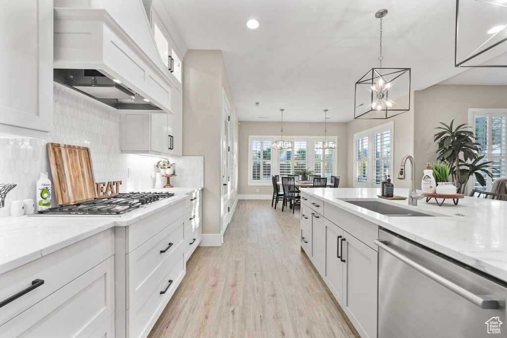 Kitchen with appliances with stainless steel finishes, a chandelier, custom exhaust hood, light wood-style flooring, and white cabinetry