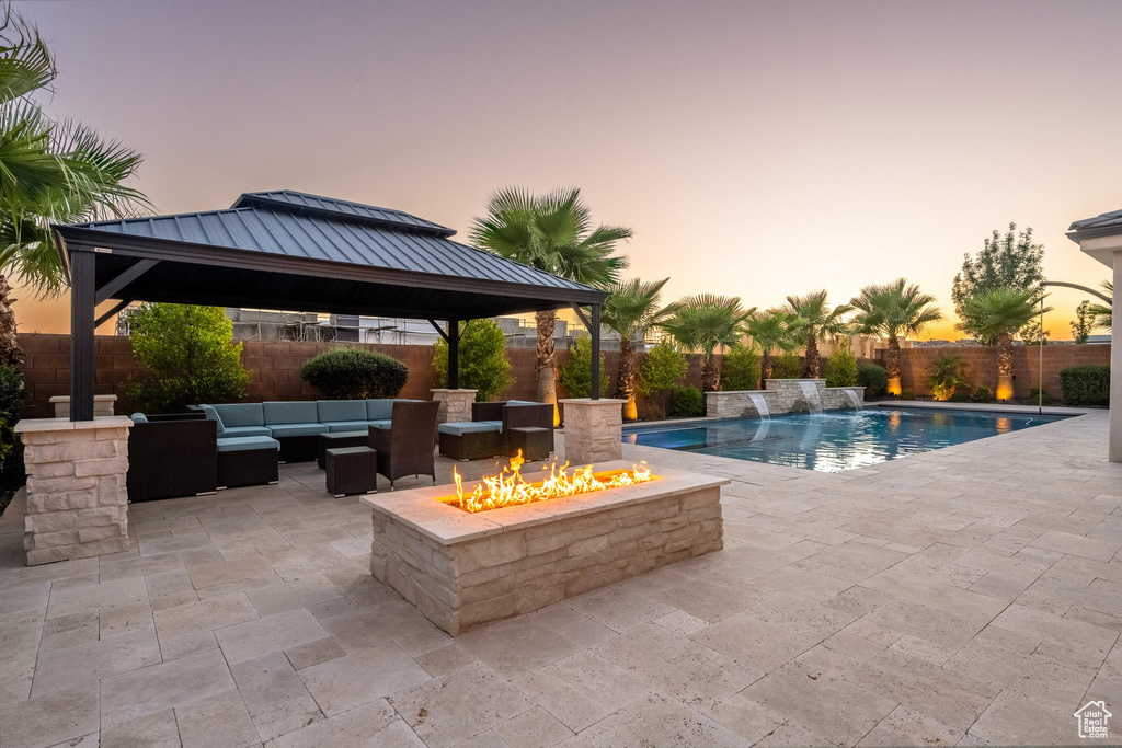 Pool at dusk featuring a gazebo, an outdoor living space with a fire pit, a patio area, and a fenced backyard