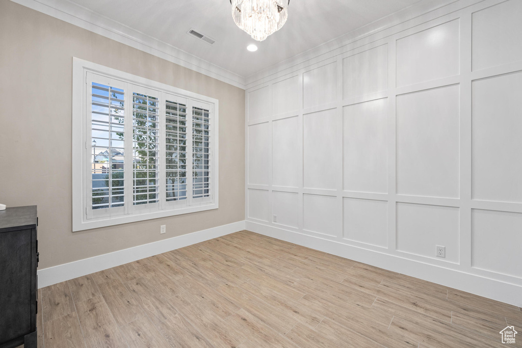 Empty room with crown molding, a decorative wall, a chandelier, and light wood-style floors