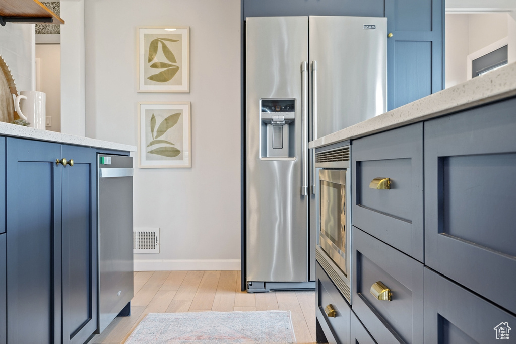Kitchen with stainless steel refrigerator with ice dispenser, light wood-type flooring, light stone counters, and blue cabinets