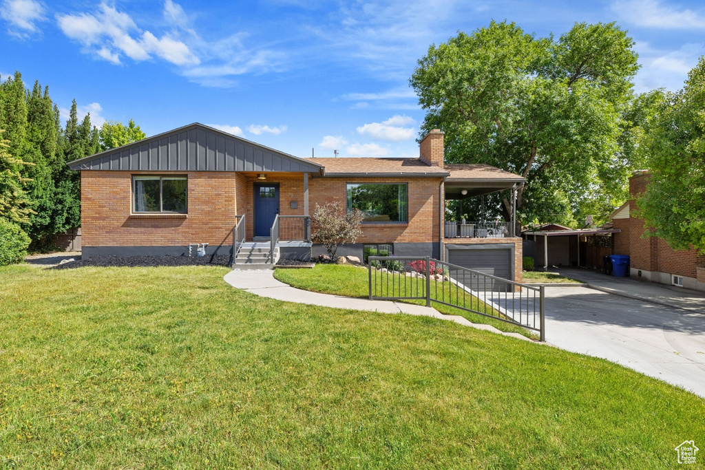 View of front facade featuring brick siding, driveway, a front yard, a chimney, and a garage
