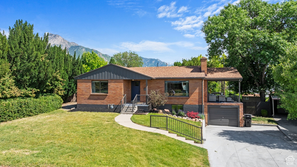 Ranch-style house with concrete driveway, a mountain view, a chimney, a garage, and brick siding