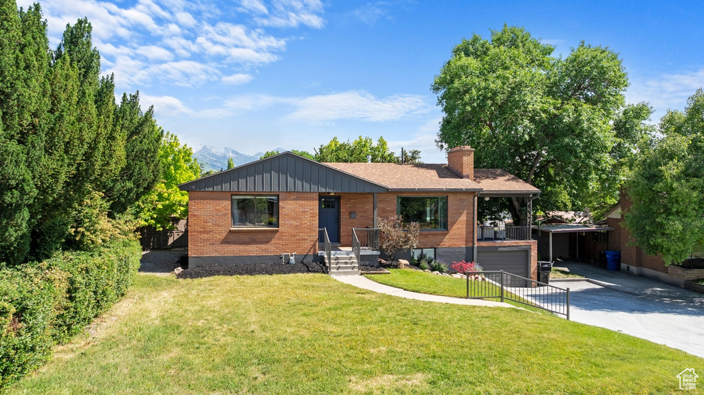 View of front of house featuring brick siding, driveway, a chimney, a front lawn, and a carport