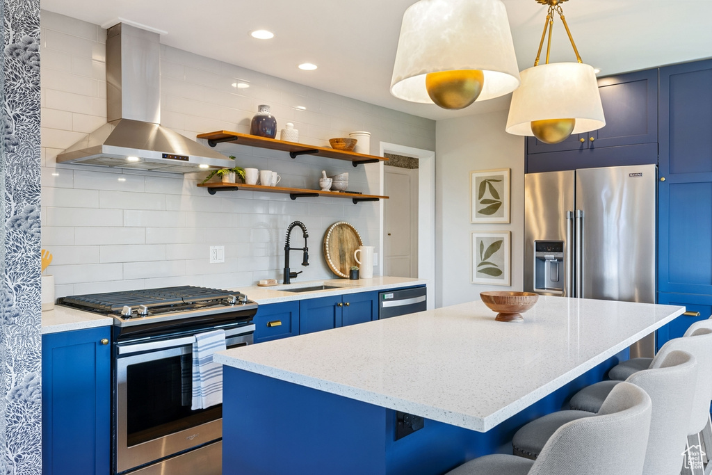 Kitchen featuring appliances with stainless steel finishes, blue cabinetry, extractor fan, a breakfast bar area, and a center island