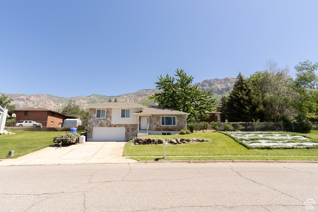 Tri-level home with stone siding, concrete driveway, a mountain view, and a garage