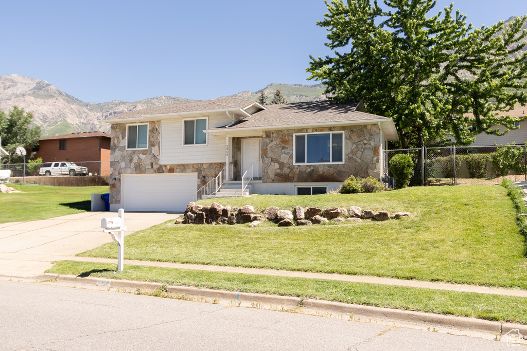 Split level home featuring stone siding, concrete driveway, an attached garage, and a mountain view