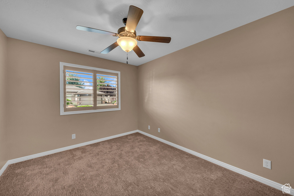 Carpeted empty room featuring ceiling fan and baseboards