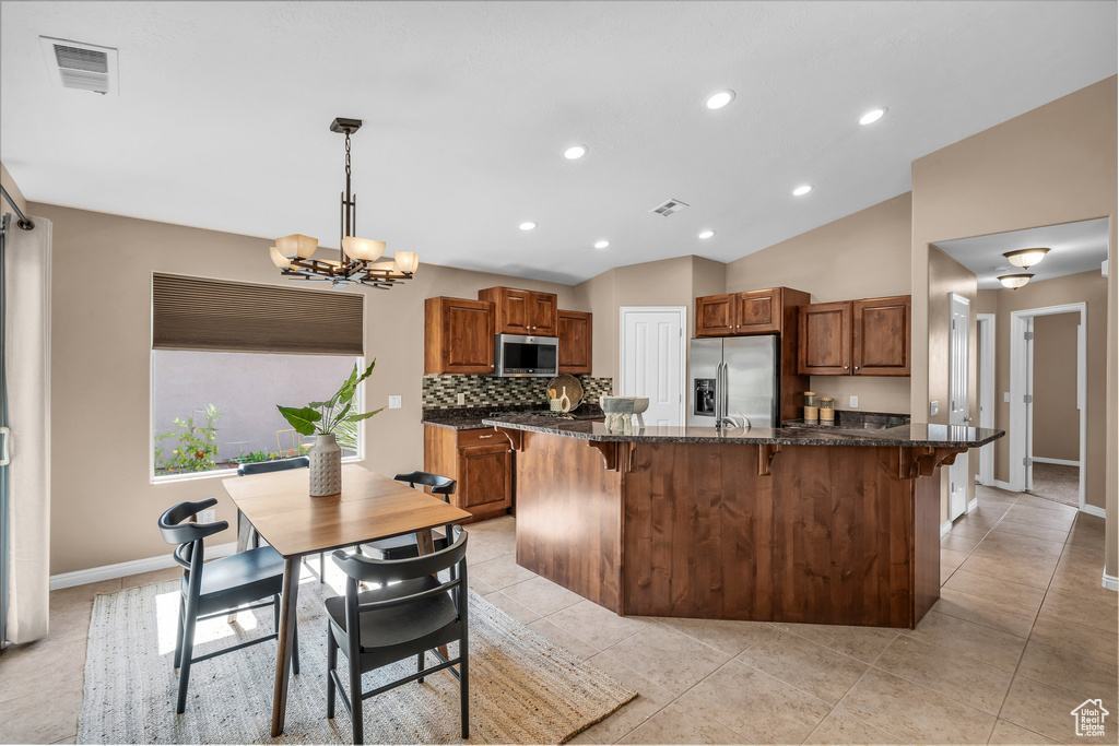 Kitchen with appliances with stainless steel finishes, a breakfast bar, brown cabinets, a chandelier, and vaulted ceiling