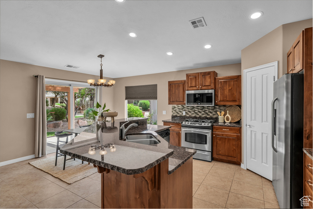 Kitchen featuring appliances with stainless steel finishes, brown cabinetry, decorative backsplash, recessed lighting, and an island with sink
