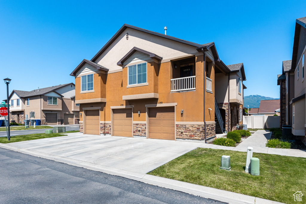 View of front of house featuring stucco siding, stone siding, an attached garage, driveway, and a front lawn