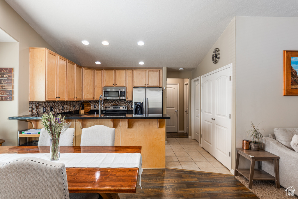 Kitchen featuring appliances with stainless steel finishes, a peninsula, backsplash, dark countertops, and a kitchen breakfast bar